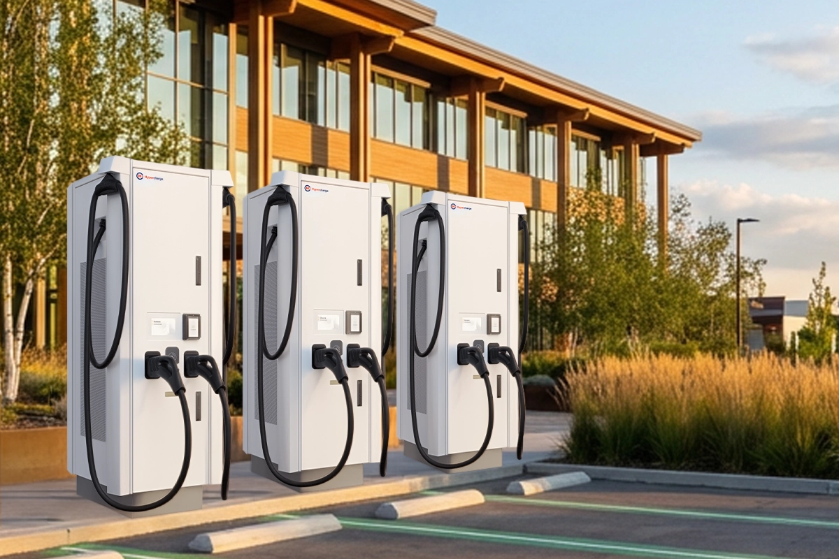 Three Hypercharge electric vehicle charging stations are installed in front of a modern office building, highlighting Ontario’s New 2026 EV Charging Rate—a big win for DC fast charging sites—with green-marked parking spaces and landscaping of trees and tall grasses in the background.